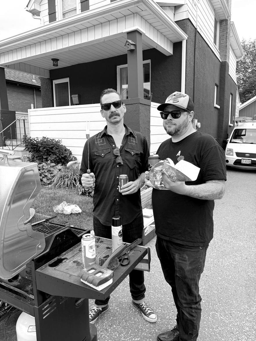 The two hosts standing at a barbecue holding hot dogs