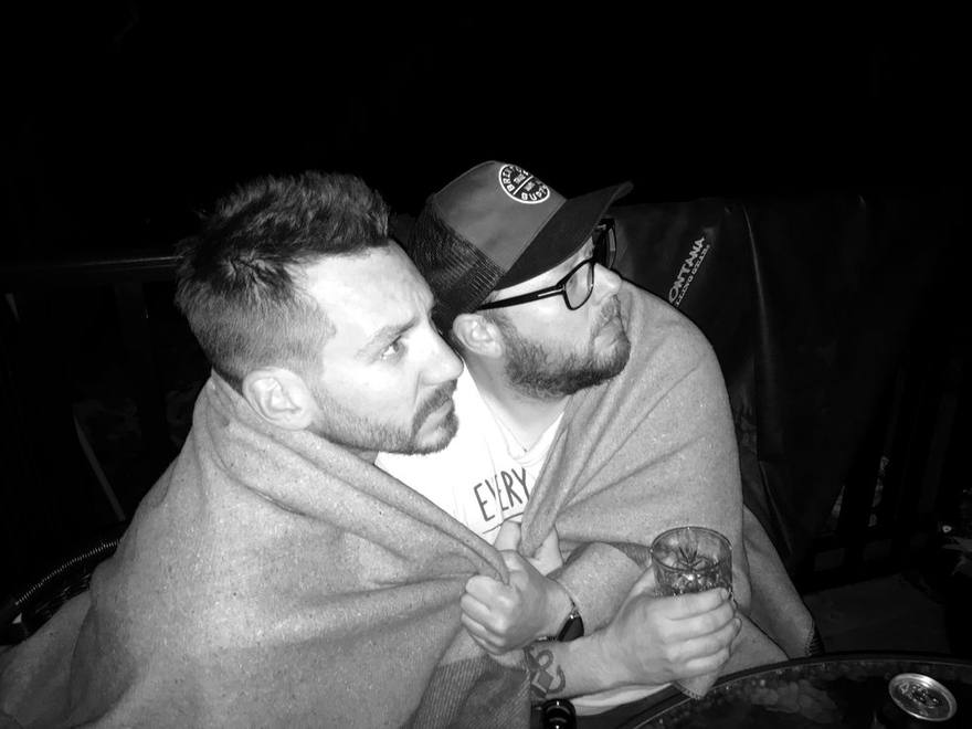 The two hosts wrapped in one blanket outdoors at night