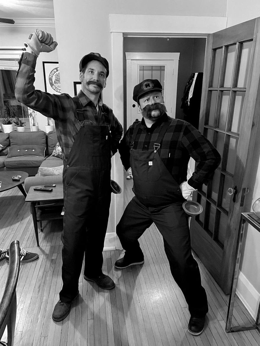 The two hosts in overalls and fake moustaches